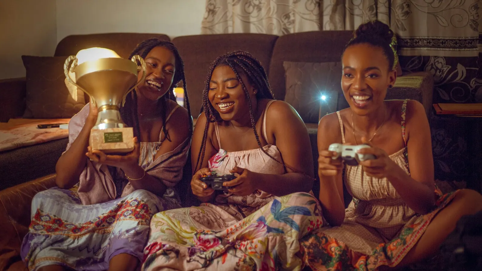 Tres amigas festejan con un trofeo mientras juegan con joysticks en el sillón